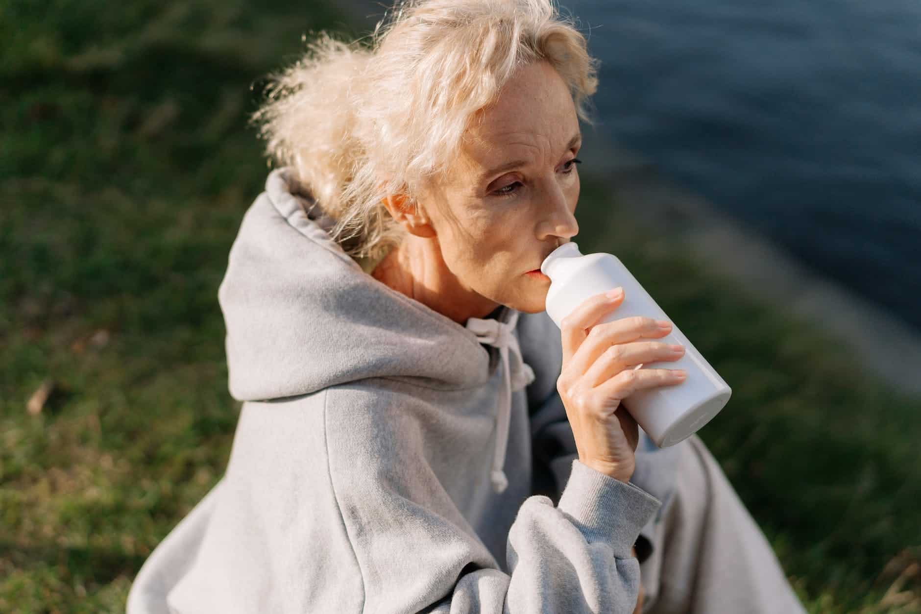 woman in gray hoodie drinking from white jar