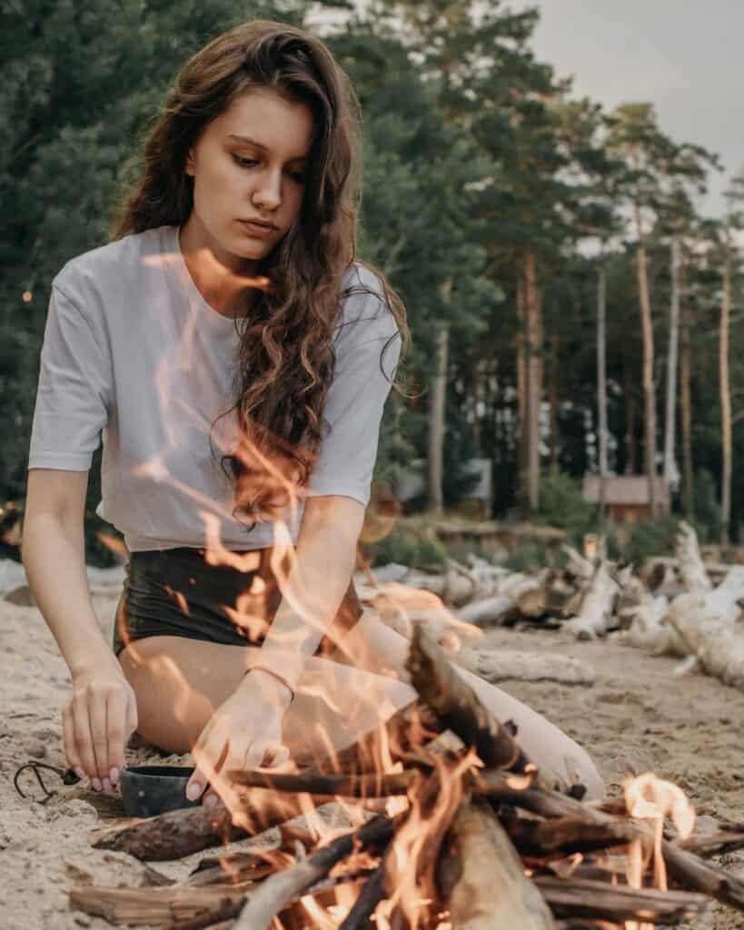 calm female sitting on sandy beach near bonfire