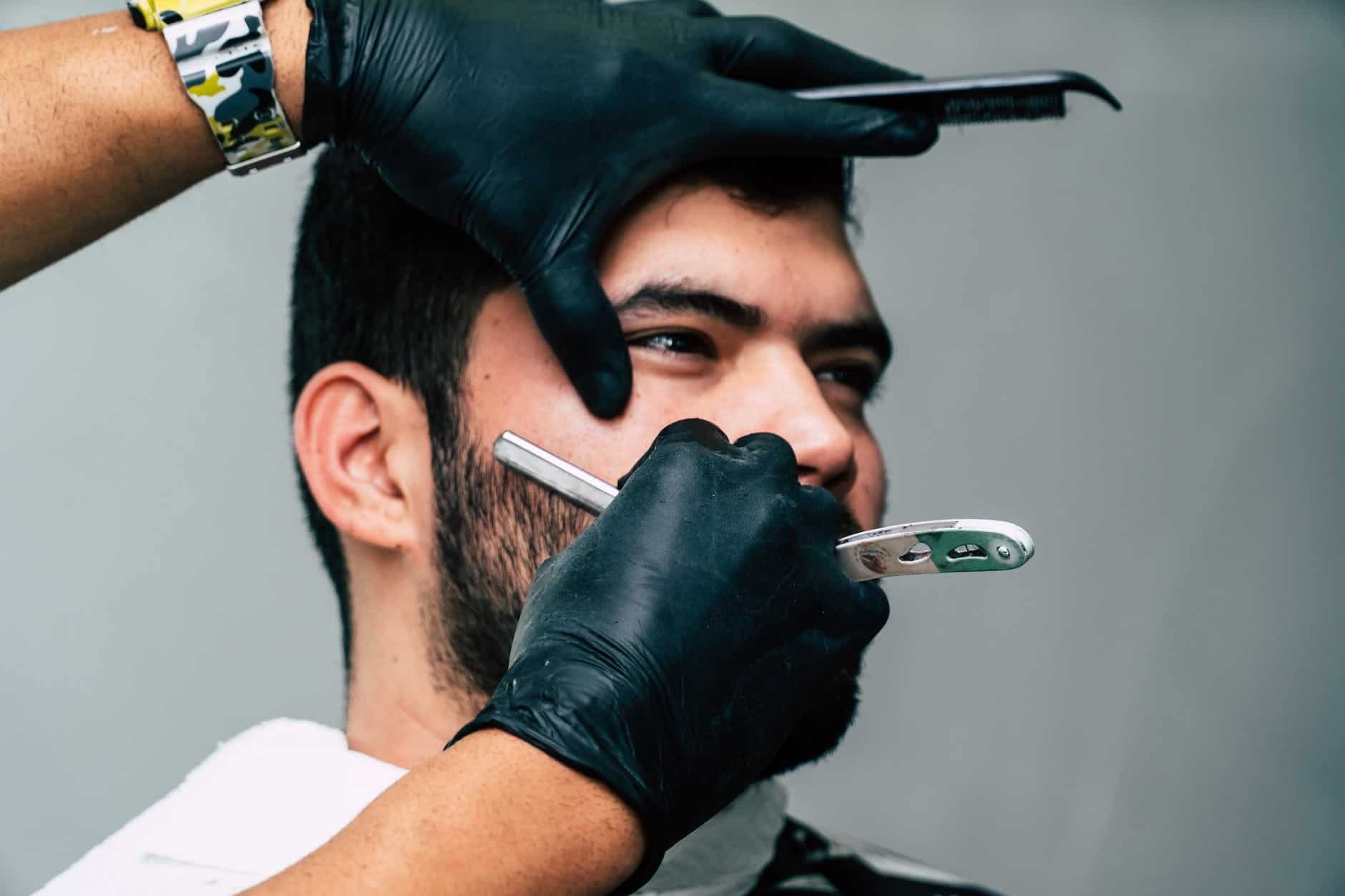 person shaving a man s face with straight razor
